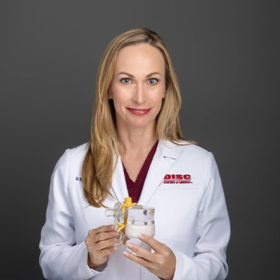 Chiropractor Ramah Wagner In Lab Coat In Front Of Grey Background